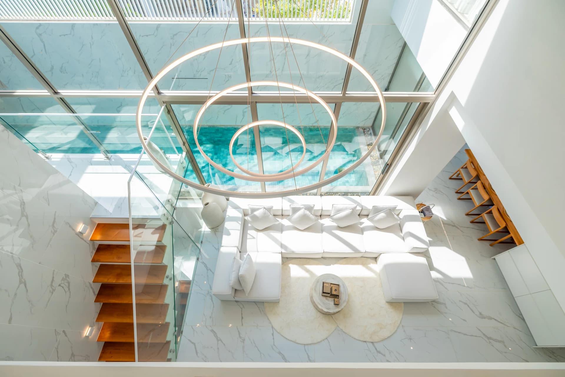 Looking down from the second floor into the double-height living room, the pool behind the glass wall