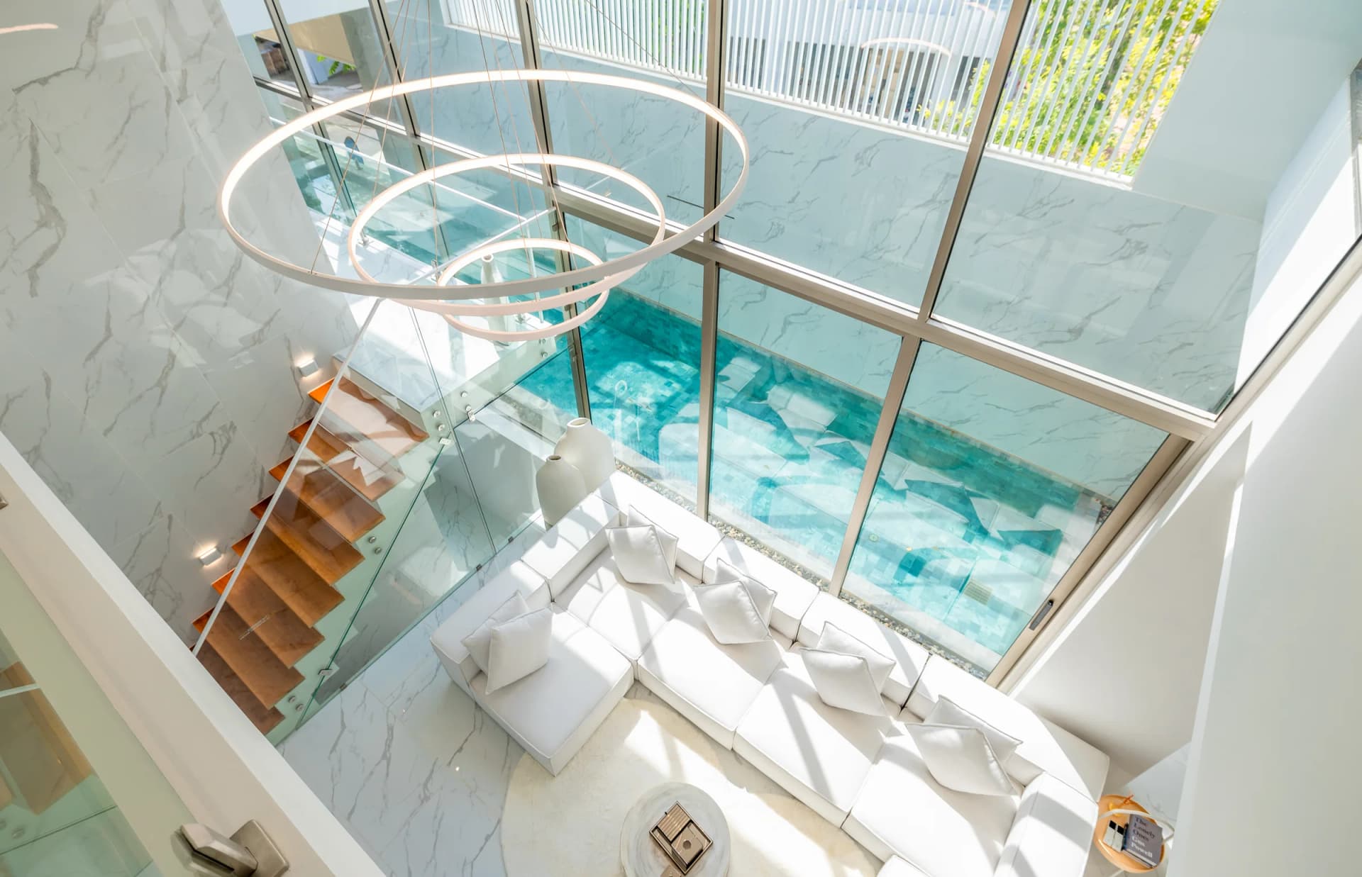 Das zweigeschossige Wohnzimmer von oben; der Pool leuchtet hinter der Glaswand